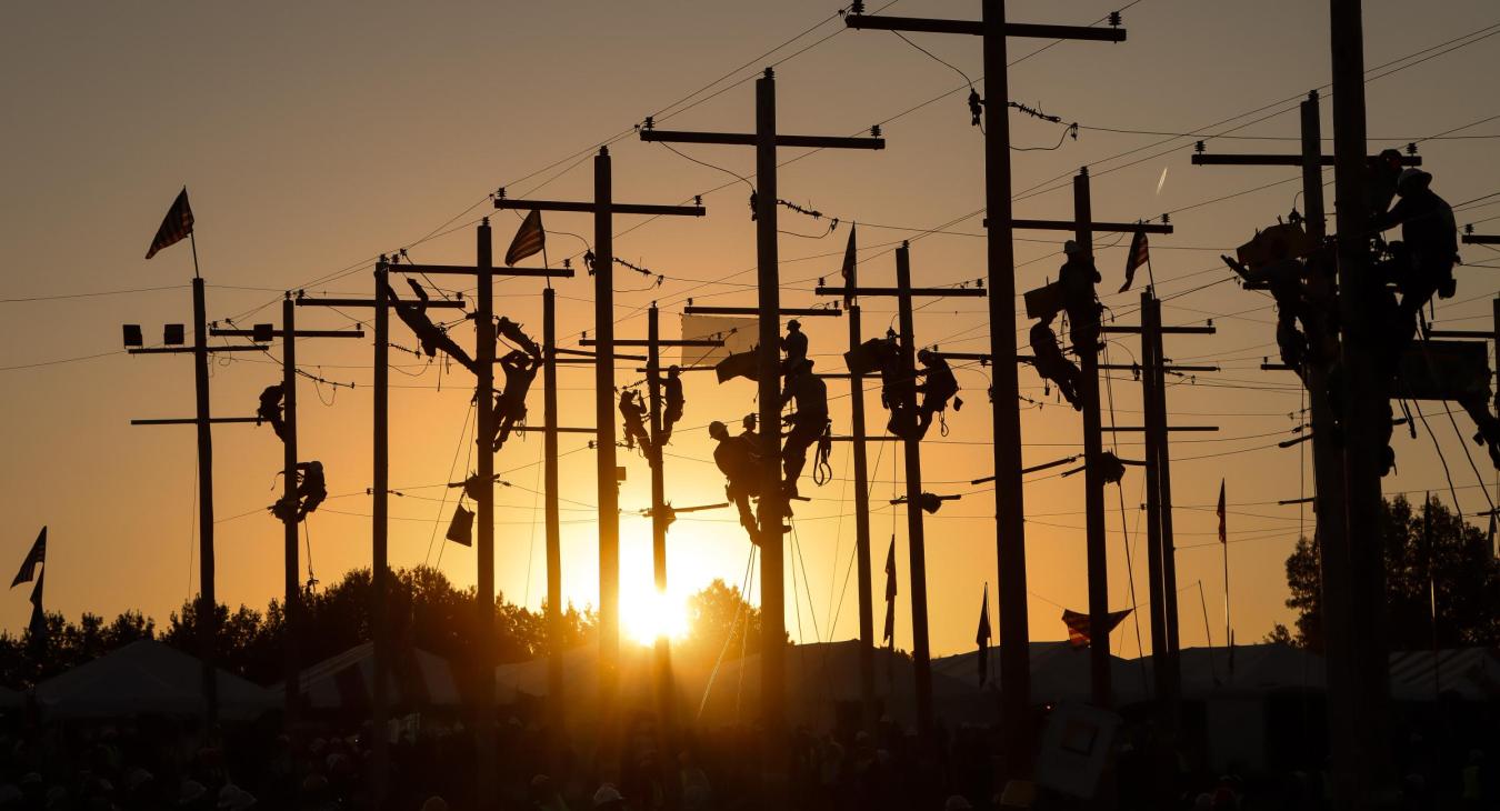 Flag ceremony featuring linemen climbing poles as the sun rises behind them